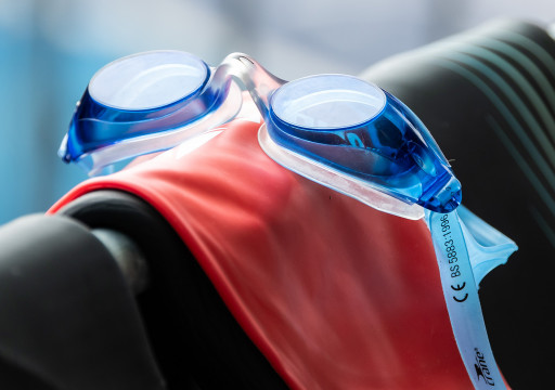 Schwimmbrille, Badekappe und Neo hängen über einem Geländer